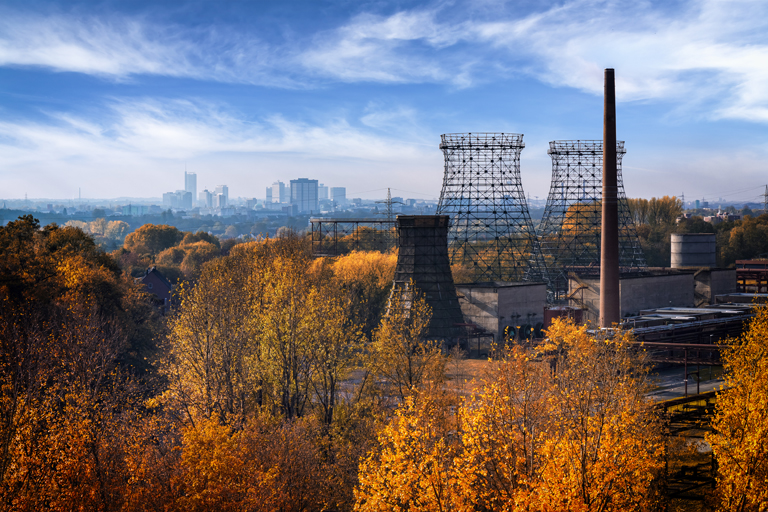 Die Zeche Zollverein umgeben von Bäumen mit buntem Herbstlaub, im Hintergrund die Essener City