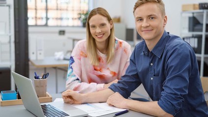 Zwei Arbeitsanfänger, die zusammen in einem Büro am Schreibtisch sitzen.