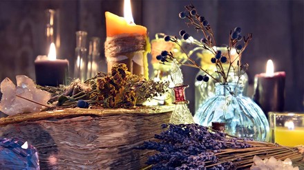 Kräuter, Kerzen, Kristalle und Blüten um Zauberbuch.