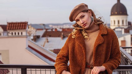 Blonde Frau vor Stadthintergrund in Teddyfell-Mantel.