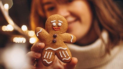 Lebkuchenmännchen, das von einer Frau im Hintergrund in die Kamera gehalten wird.