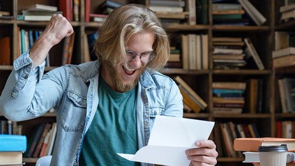 Student, der ein Blatt Papier in der Hand hält und sich über dessen Inhalt freut.