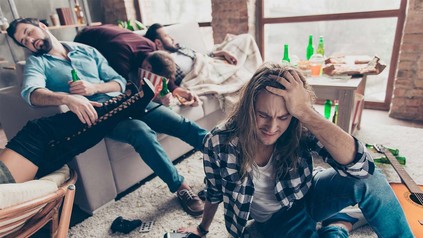 Studenten in Wohnzimmer nach Party mit Kopfschmerzen auf dem Sofa und Boden liegend umgeben von Bierflaschen.
