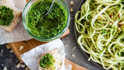 Schale mit grünem Pesto, Brot und Nudeln auf einem Tisch.
