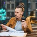 Student mit Dreadlocks sitzt mit Kaffee draußen im Cafè und lernt.