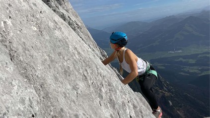 Auf dem Bild ist eine Kletterin mit Helm in den Bergen zu sehen.