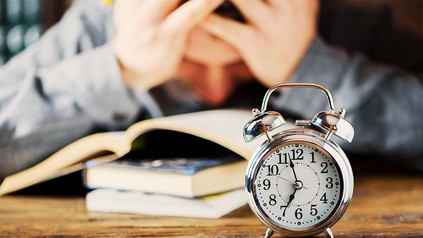 Verzweifelter Student am Schreibtisch - vor ihm eine Uhr.