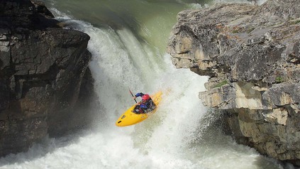Kajakfahrer auf Wildwasserstufe in einem felsigen Fluss.