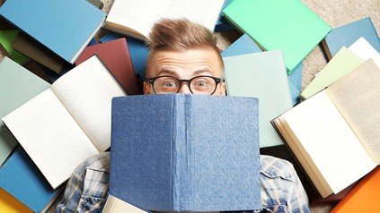Student zwischen Büchern auf dem Boden liegend.
