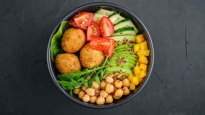 Eine hübsch angerichtete Bowl bestehend aus Mais, Tomaten, Gurken, Avocado, Falafel und Salat.