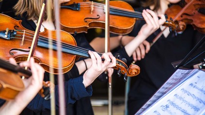 Streicherinnen im Orchester davor Notenständer mit Notenblättern.