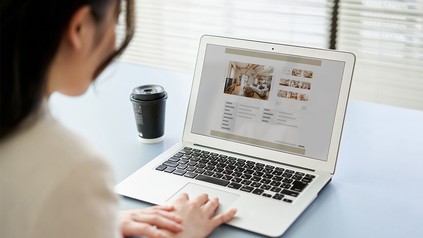 Eine junge Frau sitzt vor einem aufgeklappten Laptop und sucht nach einer passenden Wohnung.