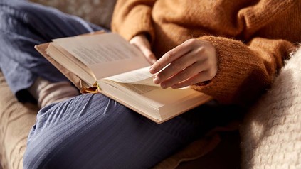 Frau in Pulli beim Lesen auf dem Sofa im Schneidersitz.