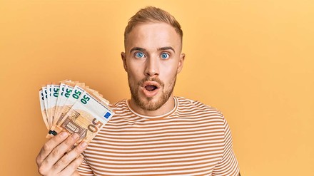 Junger Student mit offenem Mund und 50-Euro-Bündel in der Hand.