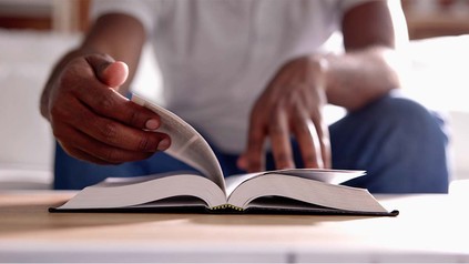 Männerhände und Buch, dass auf Tisch liegt.