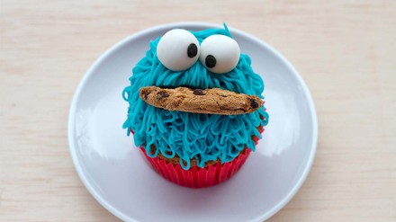 Ein Krümelmonster-Muffin auf einem weißen Teller mit einem Keks im Mund.