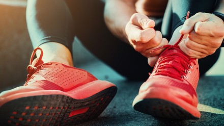 Ein Sportler schnürt seine pinken Sportschuhe im Sitzen.
