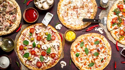 Verschiedene Pizzasorten sowie Pilze und Dips auf einem Tisch - von oben aufgenommen.