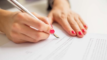 Frauenhände mit roten Nägeln, die Papier unterschreiben.