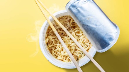 Nudel-Terrine geöffnet mit Stäbchen vor gelbem Hintergrund.