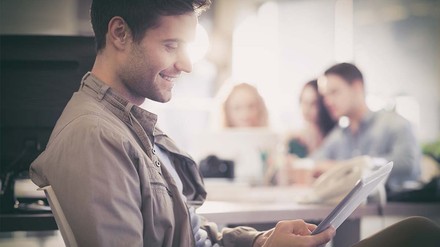 Junger Mann in Büro, der am Tablet arbeitet und lächelt.