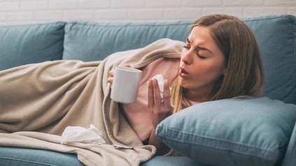 Junge blonde Frau mit Teetasse und Tempos auf Sofa.