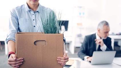 Junger Mann, der mit seinen Sachen in einem Karton das Büro verlässt.