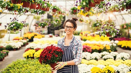 Junge Frau in Gärtnerei, die einen Blumenstock in den Händen hält und lächelt.
