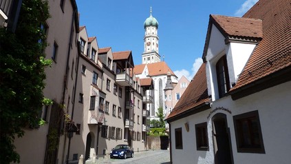 Sicht auf eine Gasse in Augsburg, im Hintergrund ist die St. Ulrichs-Kirche zu sehen.