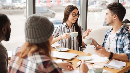 Gruppe junger Leute, die sich mit Kaffeetassen in der Hand in einem Café unterhalten.