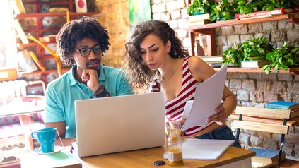 Studierende arbeiten zusammen an Laptop in einem Café.