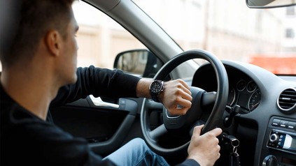 Junger Mann in Auto, der auf seine Armbanduhr blickt.