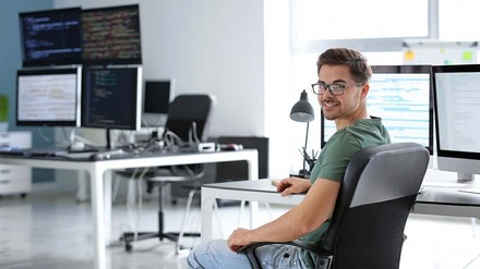 Werkstudent in der IT, der an seinem Schreibtisch sitzt und in die Kamera lächelt.