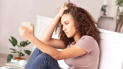 Junge, verzweifelte Frau, die auf dem Sofa sitzt und sich die Haare rauft.