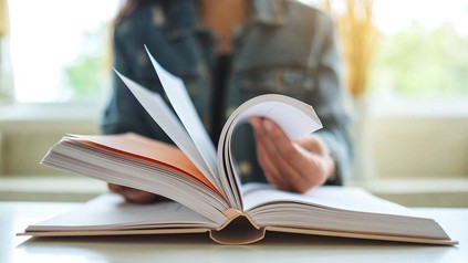 Junge Frau in Jeansjacke vor aufgeschlagenem Buch.