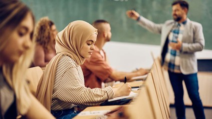 Studentin mit Kopftuch in Vorlesungsaal auf Holzbank.