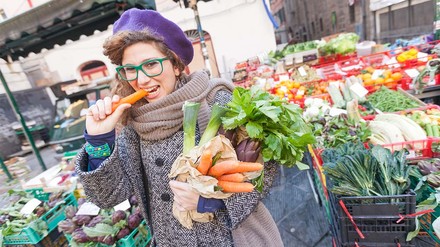 Studentin mit einer Papiertüte voller Gemüse und einer Karotte in der Hand auf dem Stadtmarkt.
