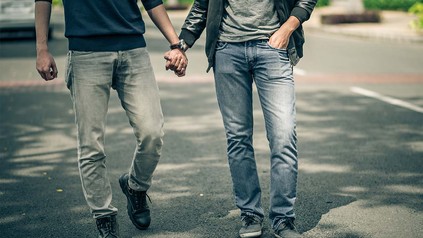 Zwei Männer, die sich bei einem Spaziergang auf der Straße an der Hand halten.