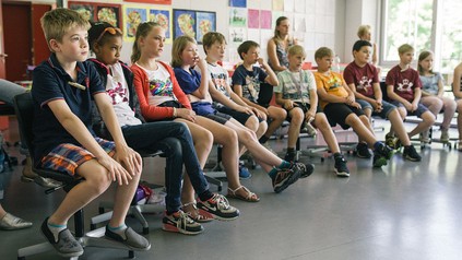 Kinder sitzen in einem Halbkreis im Klassenzimmer.