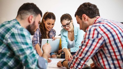 Lerngruppe von vier Studierenden, die um einen Tisch sitzen und zusammen arbeiten.