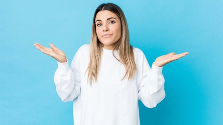 Fragt ihr euch auch manchmal: Warum? (Foto: © stock.adobe.com/Asier) Junge Frau in weißem Sweatshirt, die fragend die Arme gehoben hält, vor hellblauem Hintergrund.