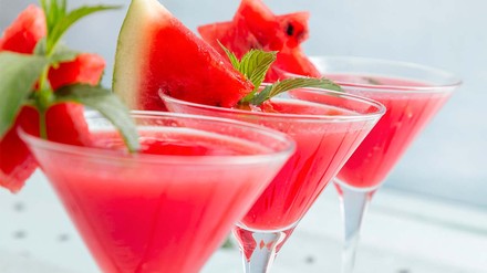 Drei Spitze Gläser voll mit Melonencocktail, jeweils verziert mit einem Stückchen Melone und frischer Minze.