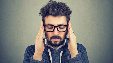 Ein erwachsener Mann mit Bart fasst sich an den Kopf.