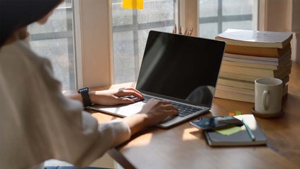 Junge Frau am Schreibtisch mit Laptop und Kaffeetasse und Notizen.
