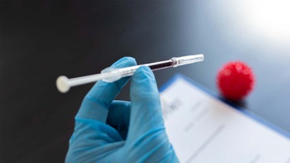 Nahaufnahme von Hand im OP-Handschuh und Blut in einer Spritze.