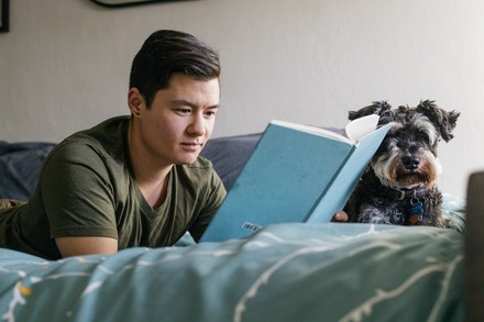 Nah am Menschen und mitten aus den Sitzungen, entwickelt sich Chungs Buch. (Foto: ©stock.adobe.com/Annie) Junger Mann im T-Shirt, der mit seinem Hund auf dem Bett liegt und liest.