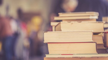 Gute Bücher musst du nicht immer neu kaufen. (Foto: © stock.adobe.com/Patrick Daxenbichler) Buchstapel auf Tisch in einem großen Raum.