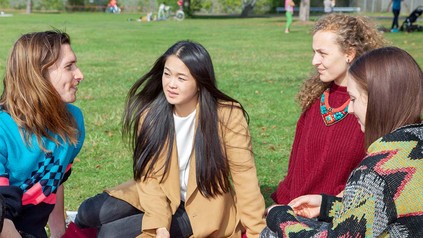 Drei junge Frauen und ein Mann, die zusammen auf einer Decke im Park sitzen und reden.