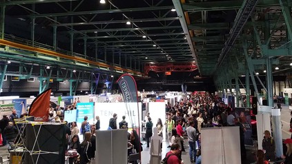 Sicht auf Messehalle mit Besuchern und Ständen.