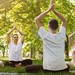 Zwei Frauen und zwei Männer im Park auf Sportmatten eine Yoga-Pose im sitzen machend.
